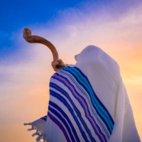 Blowing the shofar for the Feast of Trumpets - Jewish man in a traditional tallit prayer shawl blowing the ram's horn against beautiful sunset sky