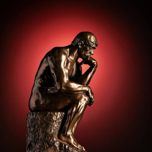 A bronze replica statue of Rodin's Thinker on a red background with vignette